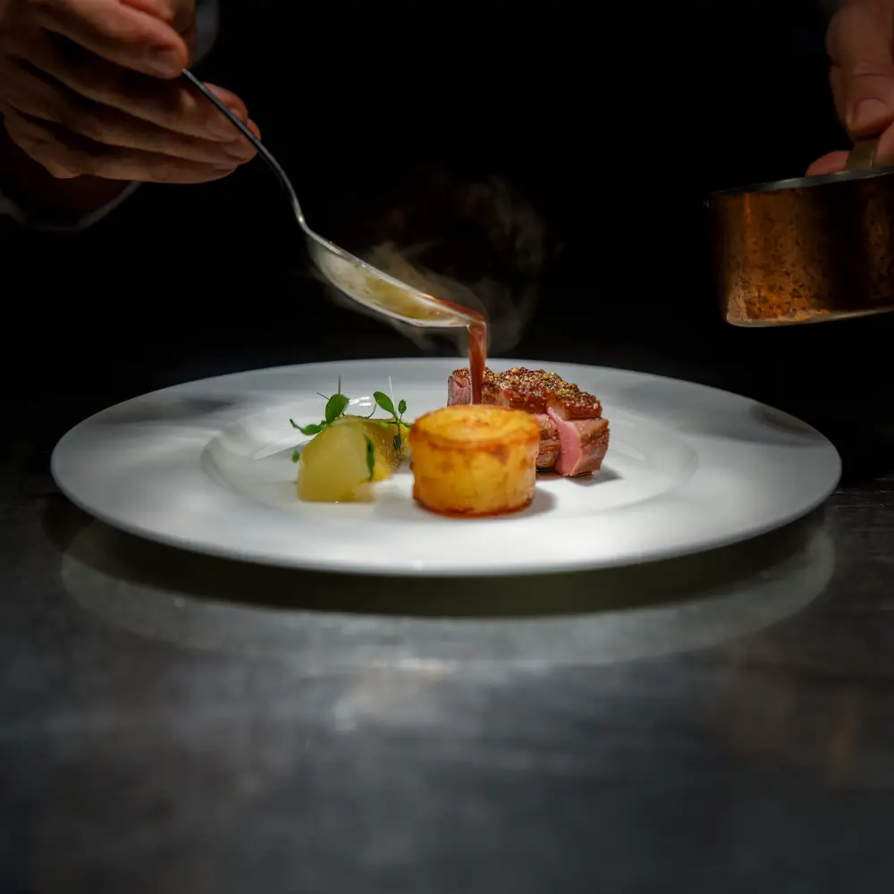 Een kok giet saus over een opgemaakt bord